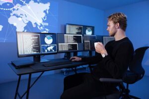 Cyber security analyst in a cyber security operations center (SOC). Multiple screens showing map, incident logs and alert data.